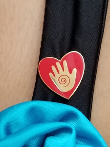 A red metalic pin with a gold hand in the center